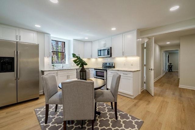 kitchen with light wood-type flooring, tasteful backsplash, stainless steel appliances, sink, and white cabinetry