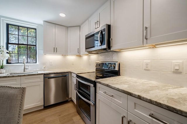 kitchen with sink, light hardwood / wood-style flooring, light stone counters, white cabinetry, and stainless steel appliances