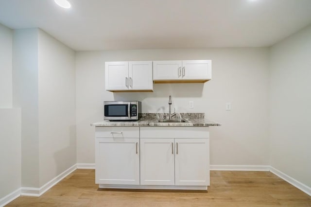 kitchen with white cabinets, light wood-type flooring, stone countertops, and sink