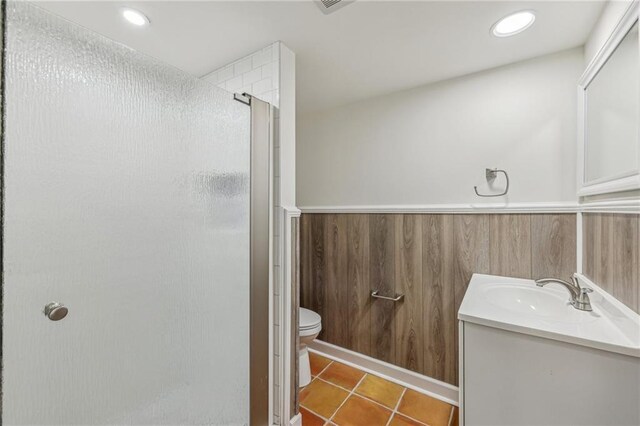 bathroom featuring vanity, wooden walls, tile patterned floors, walk in shower, and toilet