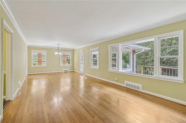 spare room featuring an inviting chandelier, crown molding, and light hardwood / wood-style floors