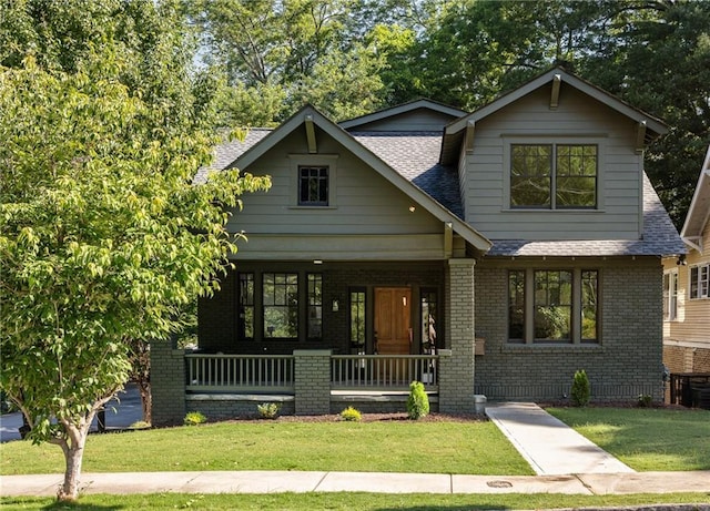 craftsman-style home featuring covered porch, roof with shingles, brick siding, and a front lawn