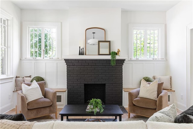 living room with a brick fireplace, a decorative wall, and wood finished floors