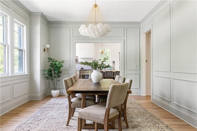 dining area with light wood-style flooring, a decorative wall, and a notable chandelier