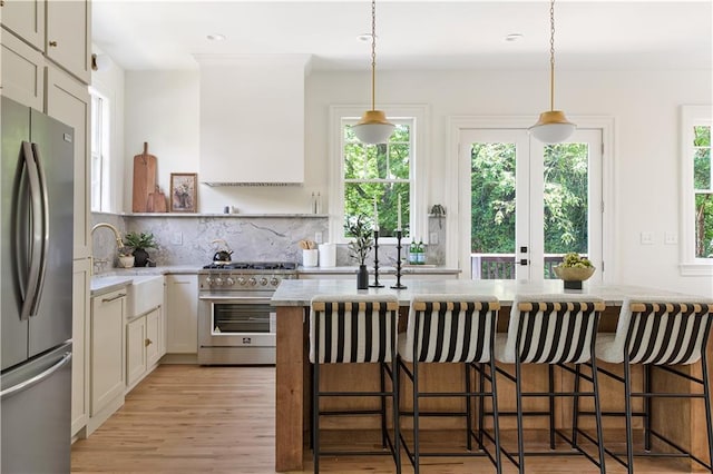 kitchen featuring light wood finished floors, tasteful backsplash, custom range hood, appliances with stainless steel finishes, and a sink