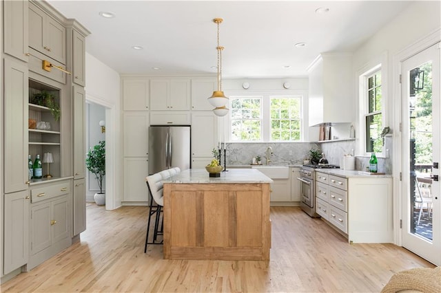 kitchen featuring light wood finished floors, decorative backsplash, a kitchen island, appliances with stainless steel finishes, and open shelves