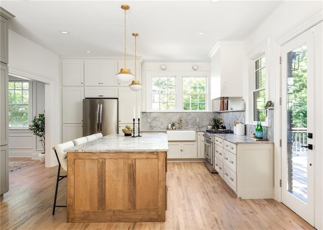 kitchen featuring a center island, light wood finished floors, tasteful backsplash, appliances with stainless steel finishes, and a sink