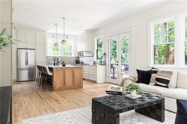 kitchen with stainless steel refrigerator, open floor plan, light countertops, light wood-type flooring, and backsplash