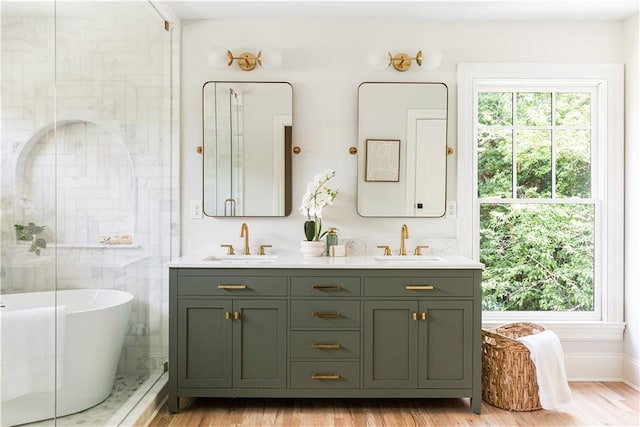 bathroom with double vanity, a freestanding tub, a sink, and wood finished floors