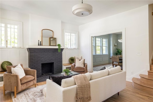 living room with stairway, a brick fireplace, wood finished floors, and a decorative wall