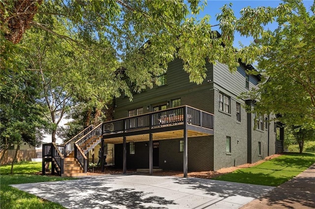 exterior space featuring brick siding, driveway, stairway, a wooden deck, and a front lawn