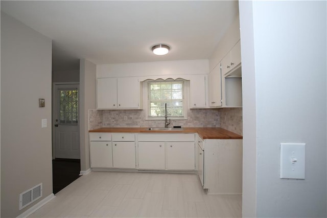 kitchen featuring visible vents, butcher block countertops, a sink, white cabinetry, and backsplash