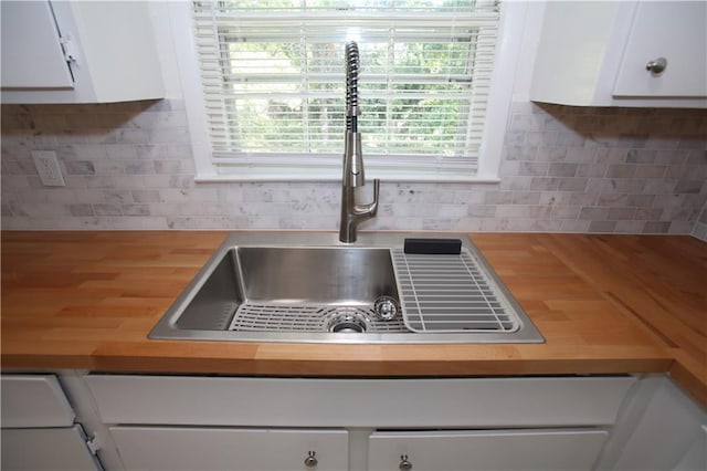 interior details with a sink, tasteful backsplash, butcher block counters, and white cabinetry