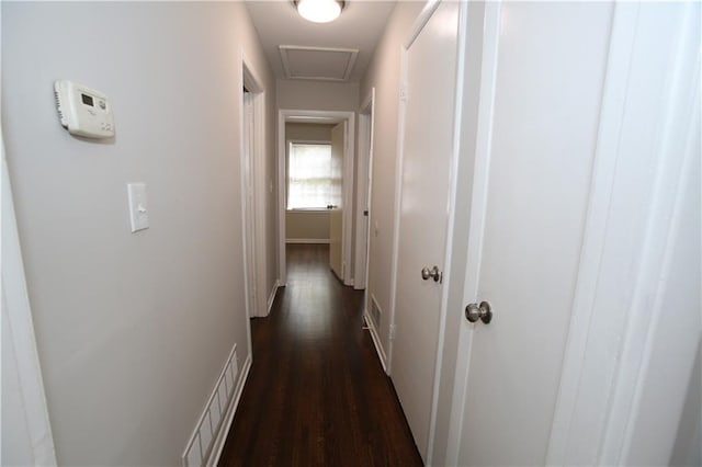 hallway featuring dark wood finished floors, visible vents, attic access, and baseboards