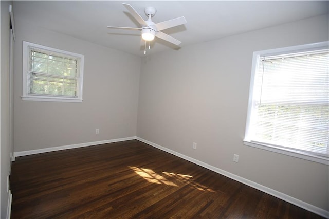 empty room featuring plenty of natural light, dark wood-type flooring, and baseboards