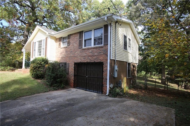 view of side of home featuring brick siding, fence, a lawn, a garage, and driveway