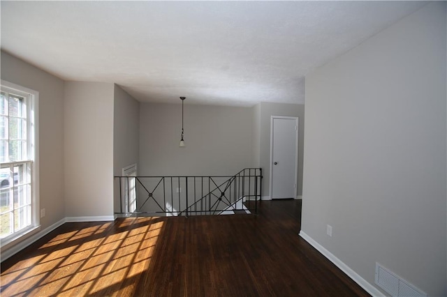 unfurnished room featuring a wealth of natural light, visible vents, baseboards, and wood finished floors