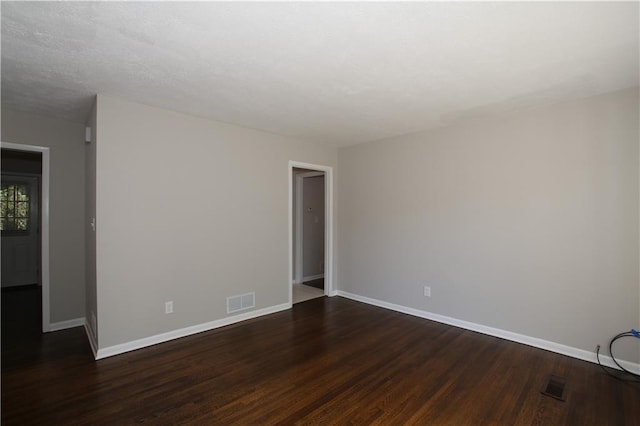 empty room with dark wood finished floors, baseboards, and visible vents