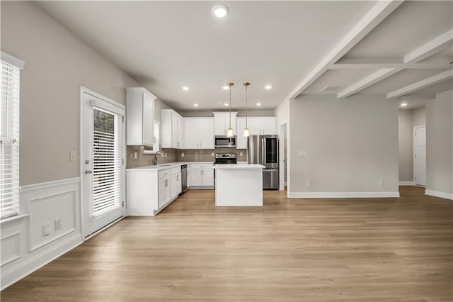 kitchen with sink, appliances with stainless steel finishes, white cabinetry, a kitchen island, and decorative light fixtures