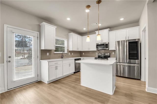 kitchen with pendant lighting, sink, white cabinetry, stainless steel appliances, and a center island