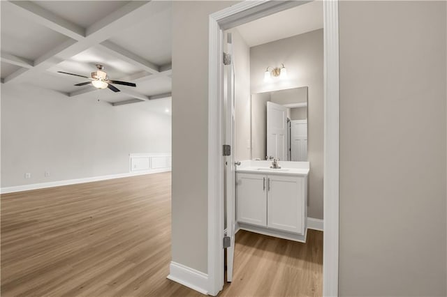 hall featuring beamed ceiling, coffered ceiling, sink, and light hardwood / wood-style flooring