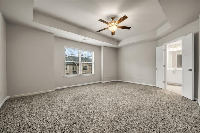 empty room with ceiling fan, light colored carpet, and a raised ceiling