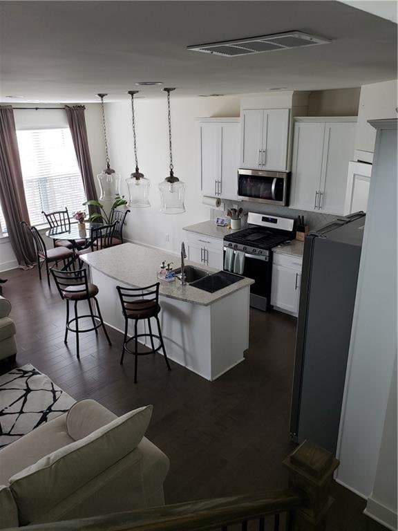 kitchen with white cabinetry, appliances with stainless steel finishes, a kitchen island with sink, dark hardwood / wood-style floors, and pendant lighting