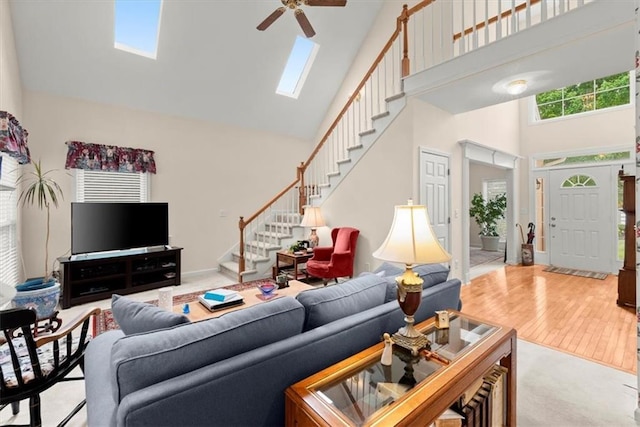 living room with a towering ceiling, ceiling fan, light hardwood / wood-style floors, and a skylight