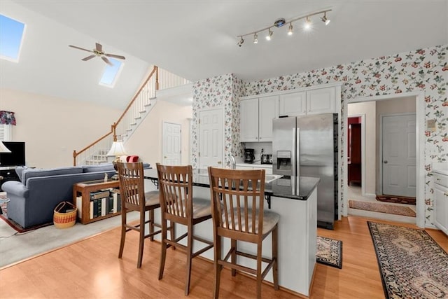 kitchen featuring a kitchen breakfast bar, light hardwood / wood-style floors, stainless steel fridge with ice dispenser, ceiling fan, and white cabinetry