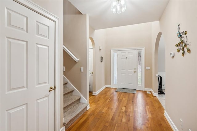 entrance foyer with baseboards, arched walkways, light wood-style flooring, and stairs