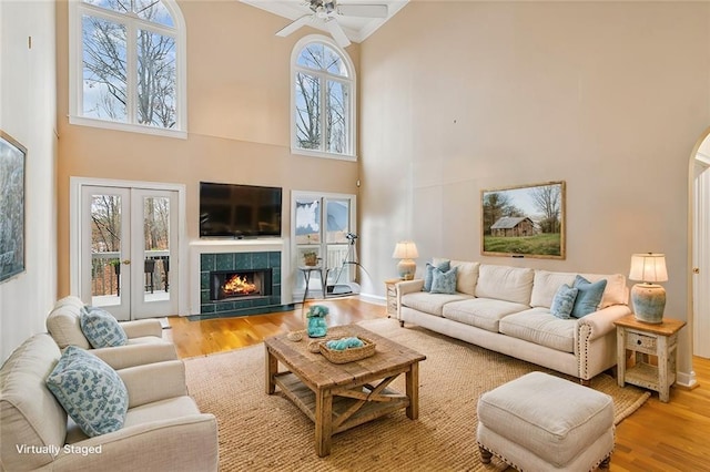 living area featuring a tile fireplace, a high ceiling, french doors, and wood finished floors