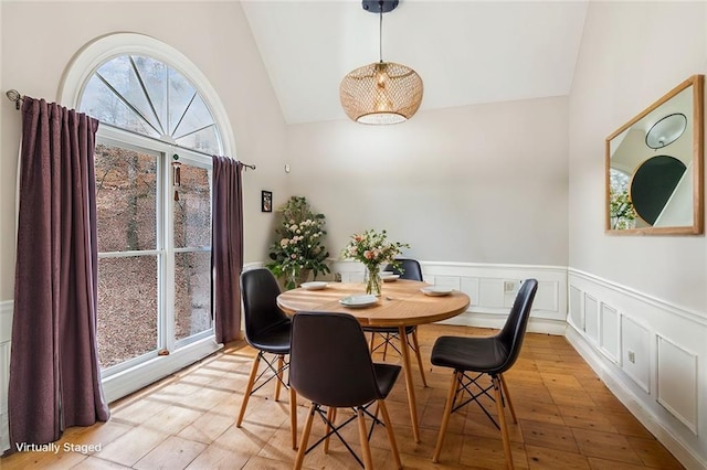 dining area featuring lofted ceiling, light wood-style flooring, a decorative wall, and wainscoting