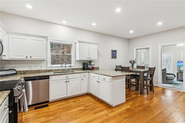 kitchen featuring a sink, white cabinetry, appliances with stainless steel finishes, a peninsula, and light wood finished floors