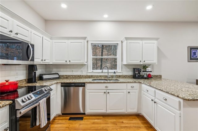 kitchen featuring light wood-style flooring, a sink, tasteful backsplash, appliances with stainless steel finishes, and a peninsula