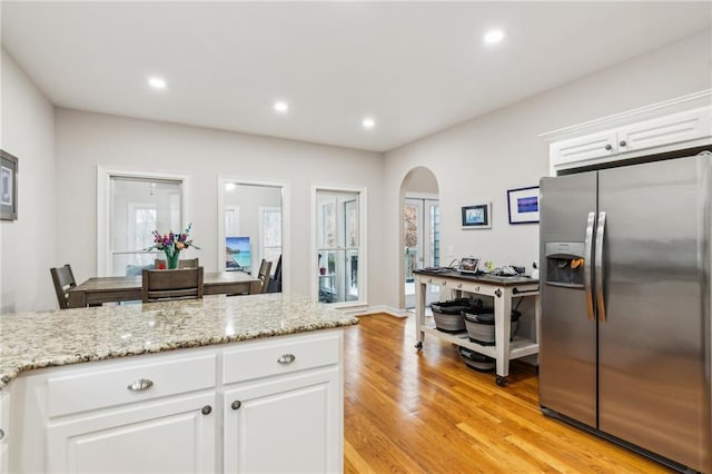 kitchen with light wood-type flooring, recessed lighting, stainless steel fridge, arched walkways, and white cabinets