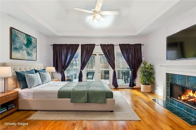 bedroom featuring a tray ceiling, wood finished floors, a tiled fireplace, and access to outside