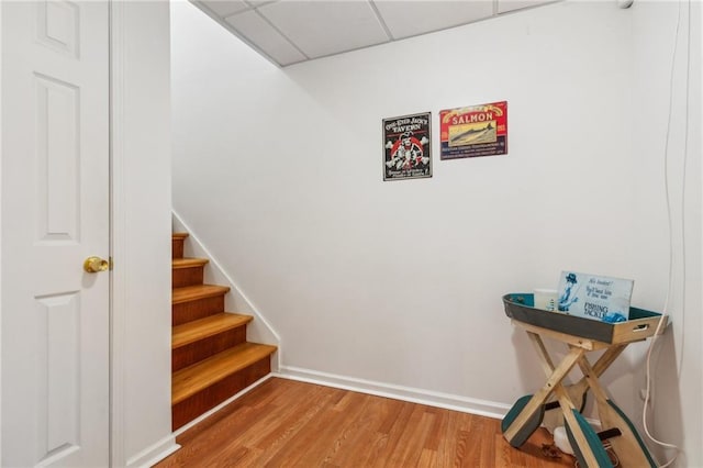 staircase featuring wood finished floors, baseboards, and a paneled ceiling