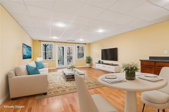 living area featuring light wood-type flooring, a paneled ceiling, baseboards, and french doors