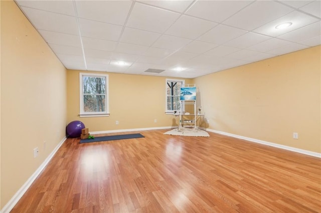 exercise area with baseboards, a paneled ceiling, and light wood-style floors