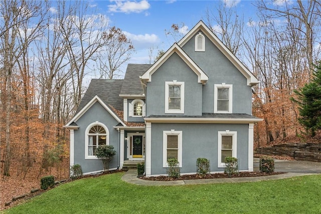 traditional-style home with stucco siding, a front lawn, and a shingled roof