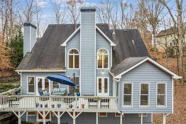 back of property with a wooden deck, french doors, a chimney, and a shingled roof