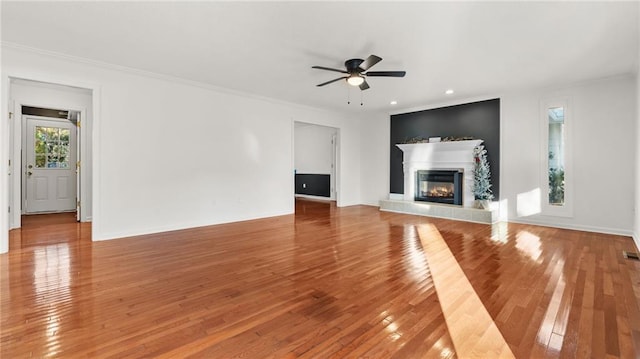 unfurnished living room with a ceiling fan, a glass covered fireplace, crown molding, and wood finished floors