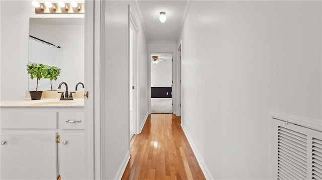 corridor featuring baseboards, a sink, visible vents, and light wood-style floors