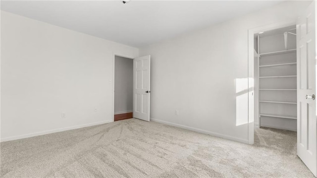 unfurnished bedroom featuring a closet, light carpet, a spacious closet, and baseboards