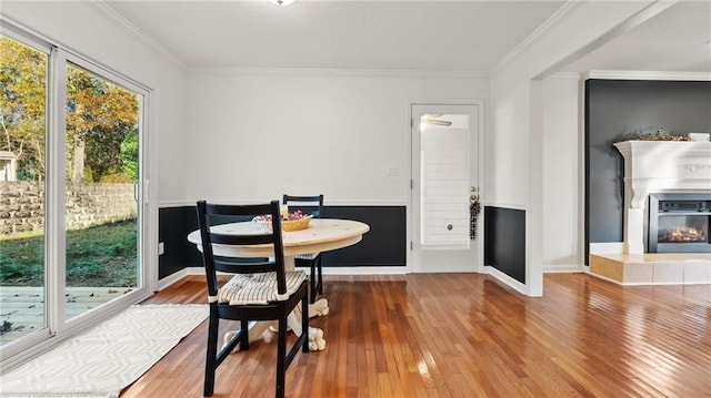 dining area featuring ornamental molding, a glass covered fireplace, wainscoting, and wood finished floors