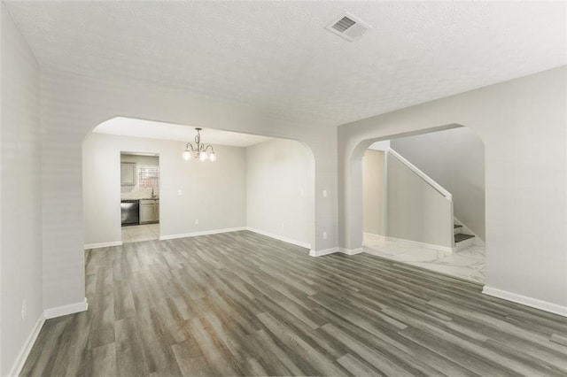 unfurnished living room featuring an inviting chandelier, dark hardwood / wood-style floors, and a textured ceiling