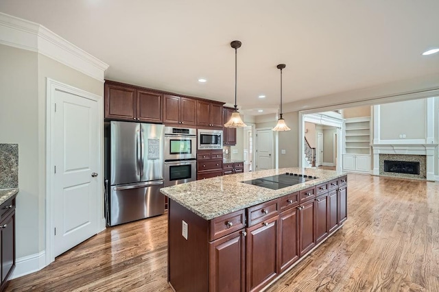 kitchen featuring hanging light fixtures, a fireplace, light stone counters, light wood finished floors, and stainless steel appliances