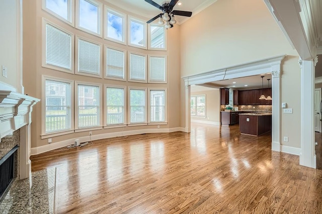 unfurnished living room featuring a ceiling fan, a high end fireplace, wood finished floors, a high ceiling, and ornamental molding