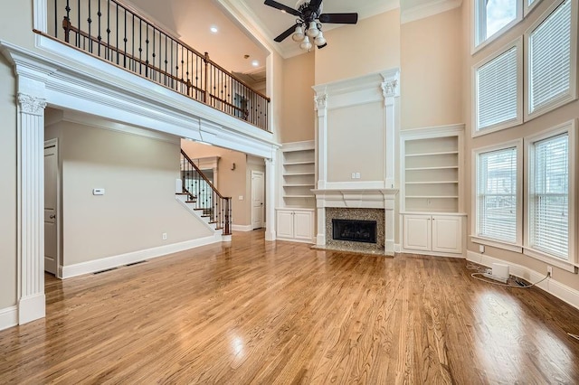 unfurnished living room with ornamental molding, a towering ceiling, a premium fireplace, and ceiling fan