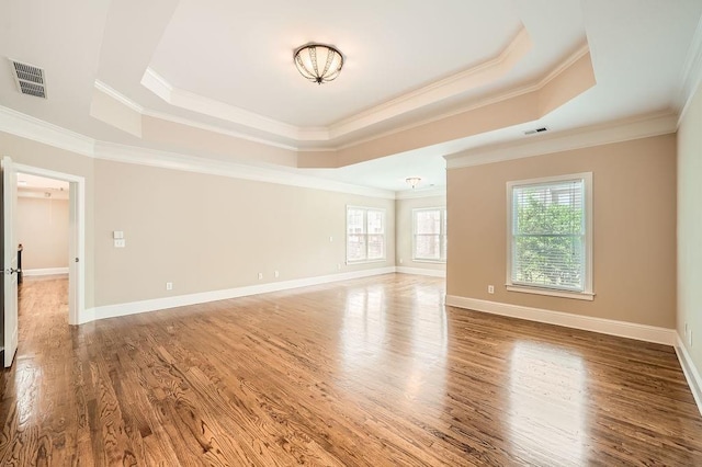unfurnished room with a tray ceiling, visible vents, ornamental molding, and wood finished floors